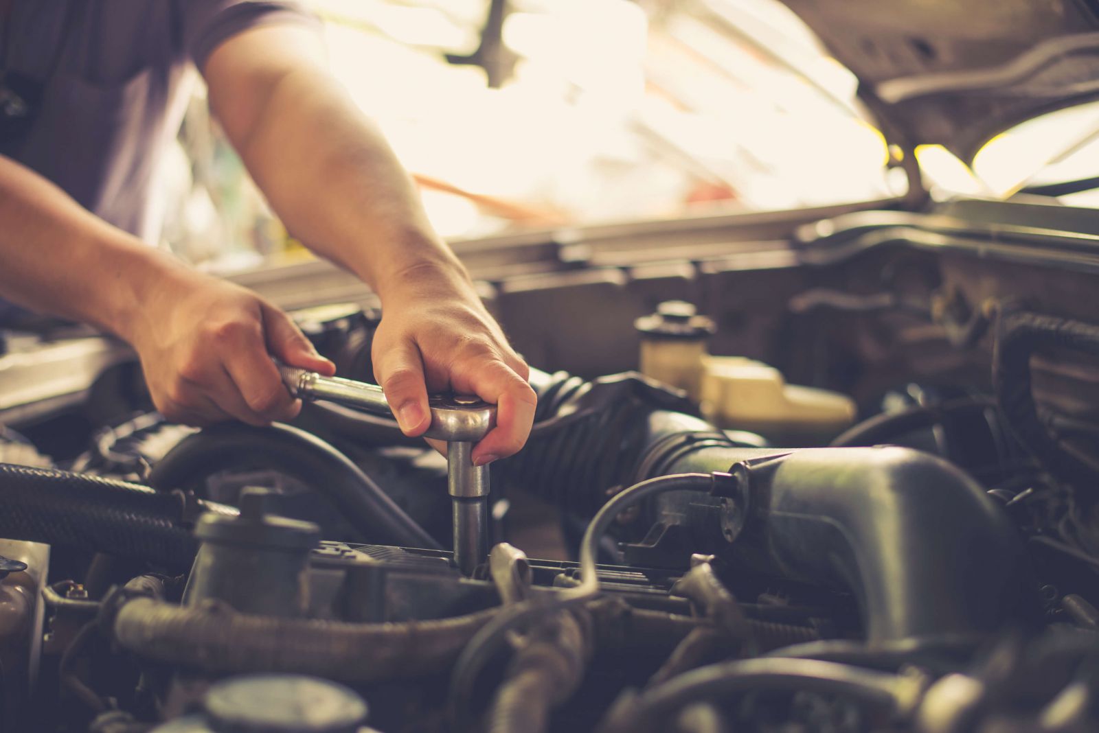 Mechanic's hands using a wrench to work on a car's engine in a garage.