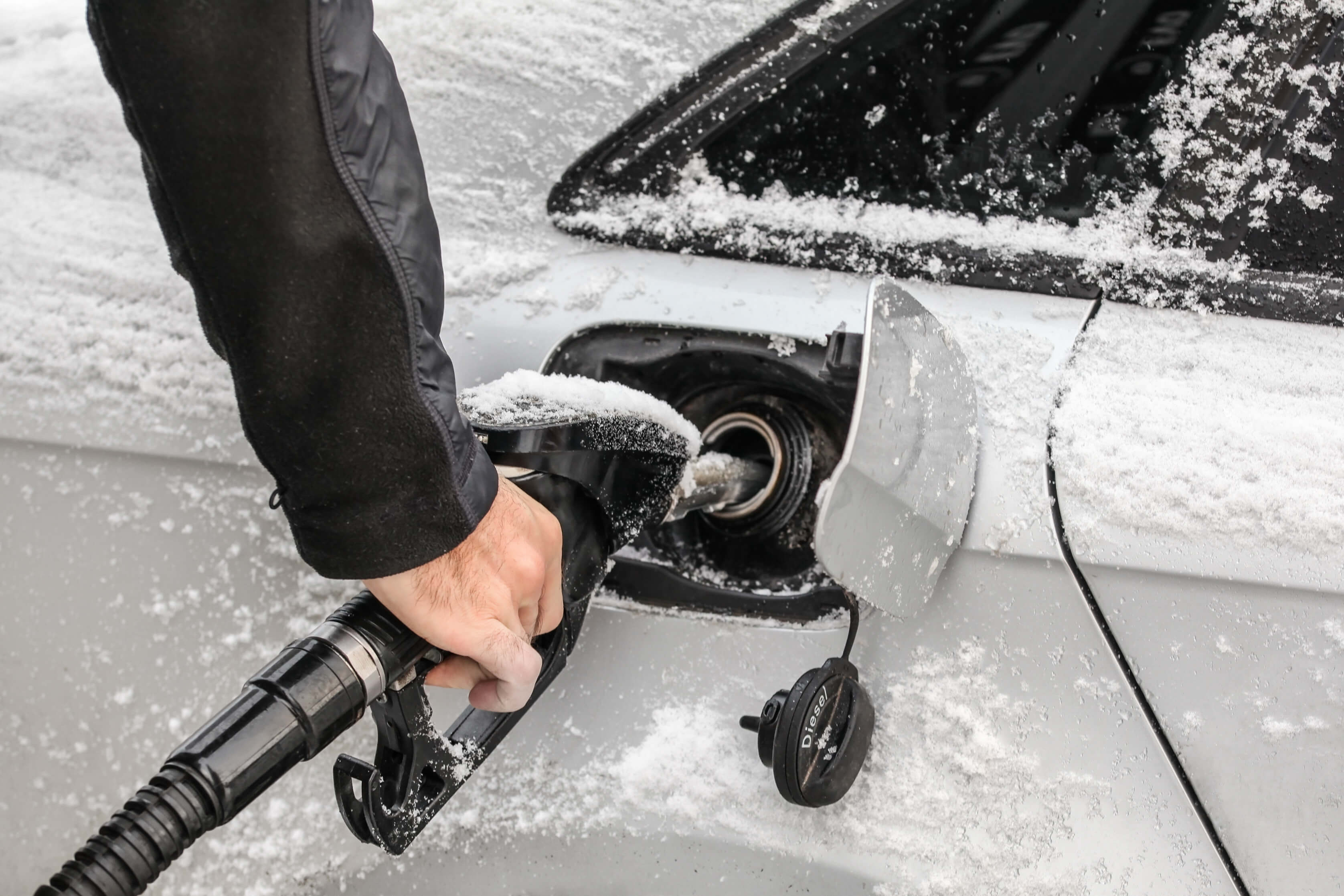 Filling gas tank of car covered with snow in winter